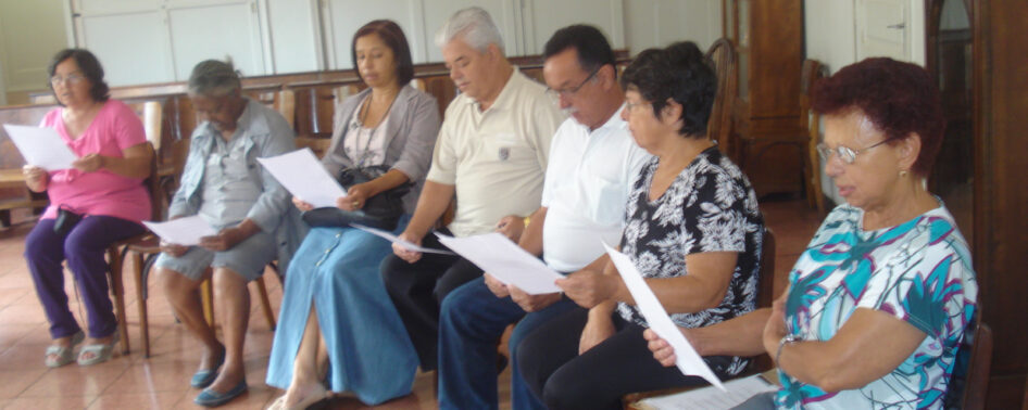 Integrantes do Grupo Irmã Maria Guedes, lado a lado, sentados em uma igreja.