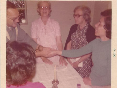Membros da comunidade Nossa Senhora das Dores orando, com uma vela sob a mesa.