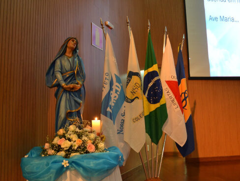 Imagem de Nossa Senhora das Dores, ao lado de quatro bandeiras. Foto do 1º Congresso de Educação da Rede Nossa Senhora das Dores.