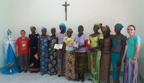 Onze mulheres da convivência vocacional em Camarões. Elas estão ao lado de uma imagem de santa. Na parede, há uma cruz.